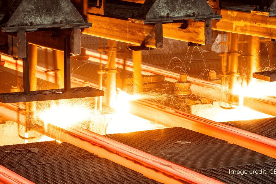 Glowing hot steel bars moving through an industrial rolling mill with bright sparks flying