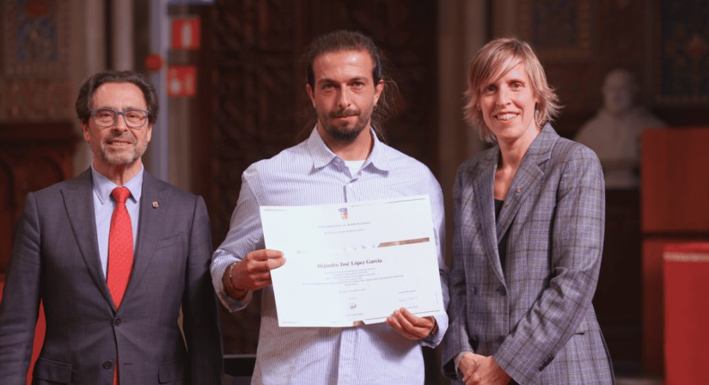 Alex Lópezholding a doctoral award certificate from the University of Barcelona, flanked by two officials in a formal hall.